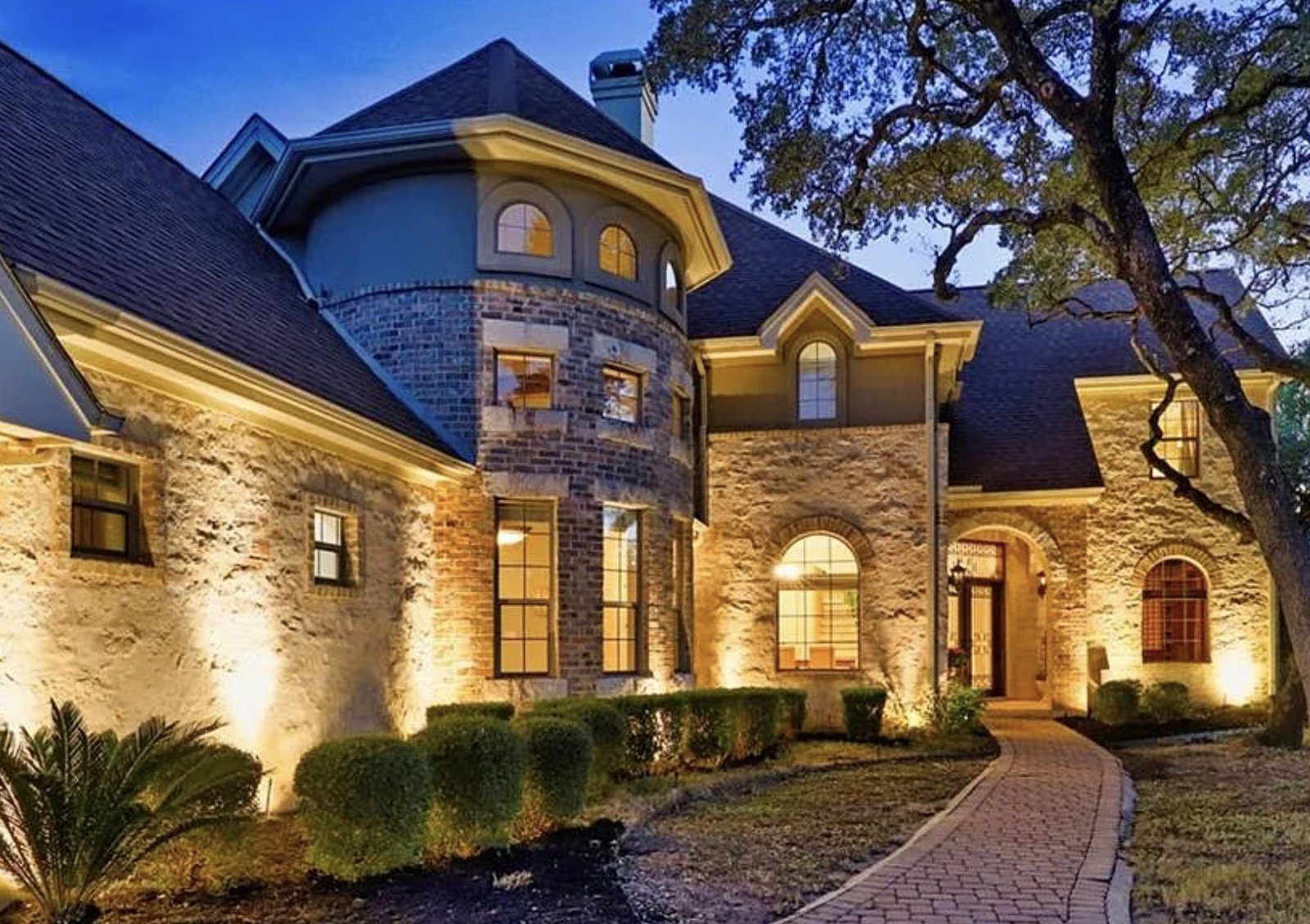 Le Petit Château at dusk, its stone turret and arched entry lit beneath a live oak